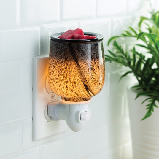 Wall-mounted wax warmer with a decorative glass cover on a tiled wall.
